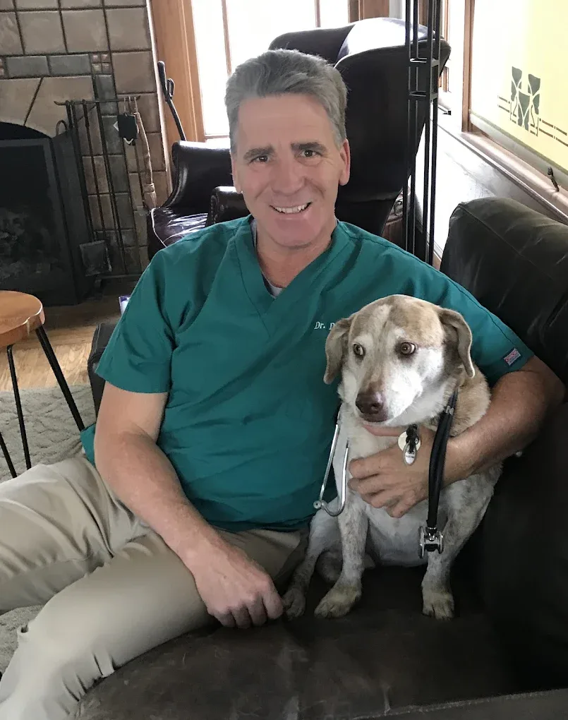 Dr. David Bennett sitting at home beside a calm senior dog during an in-home visit